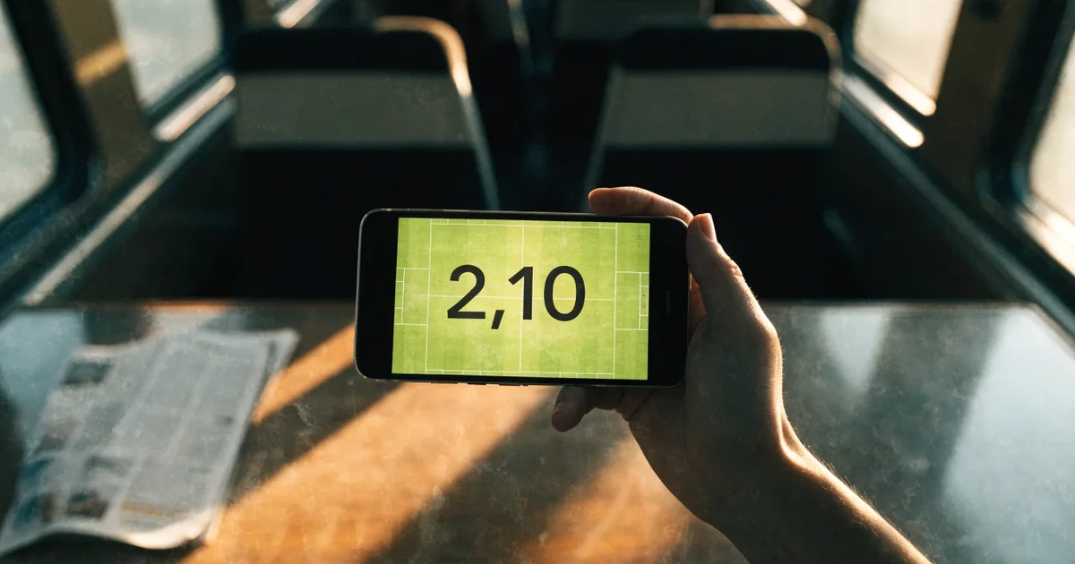 Una mano che tiene uno smartphone con una scommessa sullo schermo, su un treno nel tardo pomeriggio