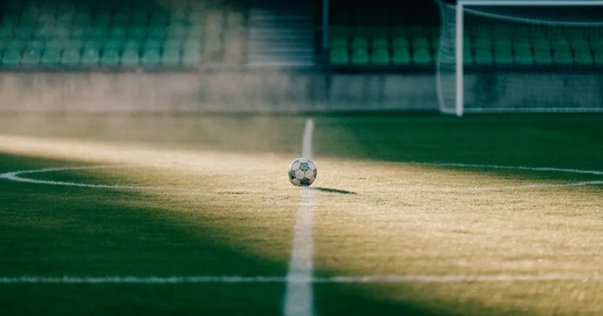 Un pallone da calcio sul dischetto del centrocampo di un prato, alla luce del mattino