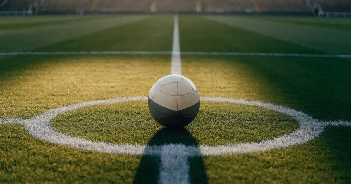 Un pallone da calcio sul dischetto del centrocampo di un prato, alla luce del mattino